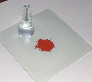 Une plaque à broyer, sa molette de verre et une terre rouge.